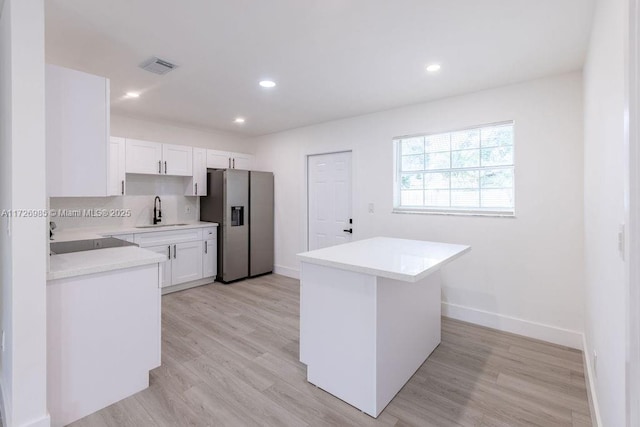 kitchen with stainless steel refrigerator with ice dispenser, sink, white cabinetry, and a kitchen island