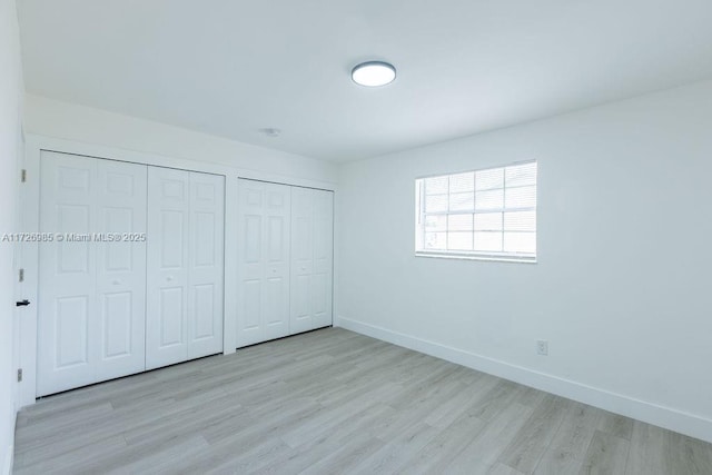 unfurnished bedroom featuring light hardwood / wood-style flooring and multiple closets