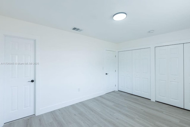 unfurnished bedroom featuring light wood-style floors, baseboards, visible vents, and two closets