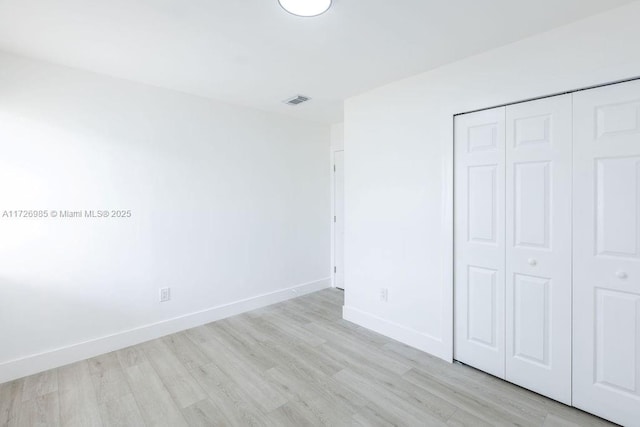 unfurnished bedroom featuring light wood-style flooring, a closet, visible vents, and baseboards