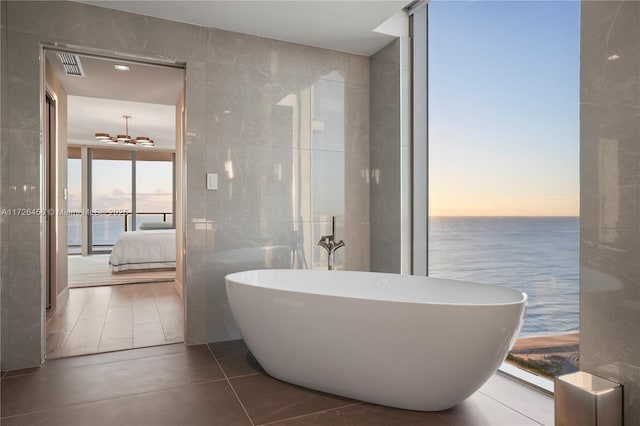 bathroom featuring visible vents, a soaking tub, tile walls, and a water view