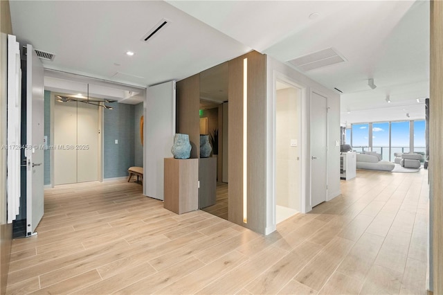 hallway with floor to ceiling windows, visible vents, and light wood-style floors