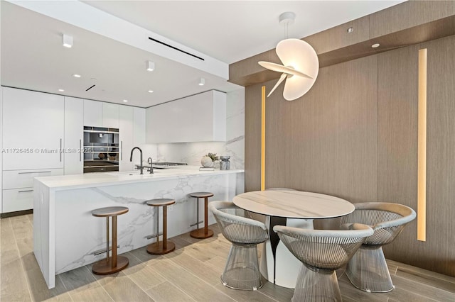 kitchen featuring a peninsula, a kitchen bar, modern cabinets, and white cabinetry