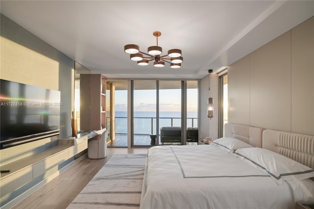 bedroom with light wood finished floors, a water view, access to exterior, a wall of windows, and a chandelier