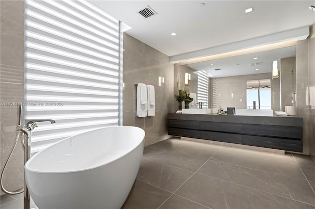 bathroom featuring a soaking tub, visible vents, tile walls, and double vanity