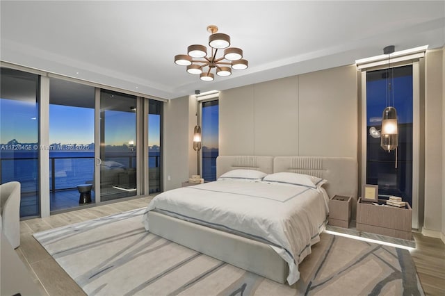 bedroom featuring a water view, a notable chandelier, access to outside, and wood finished floors