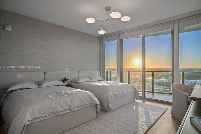 bedroom featuring wallpapered walls, a wall of windows, wood finished floors, and access to exterior