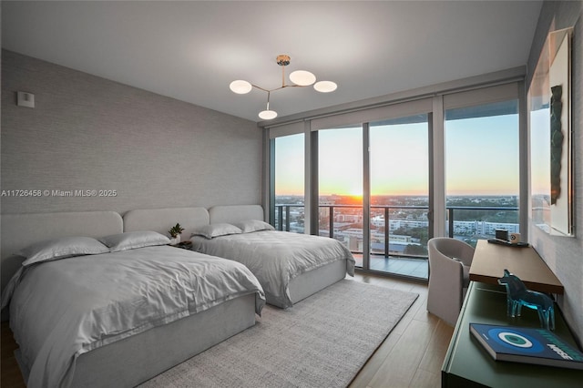 bedroom featuring access to outside, floor to ceiling windows, a view of city, light wood finished floors, and wallpapered walls