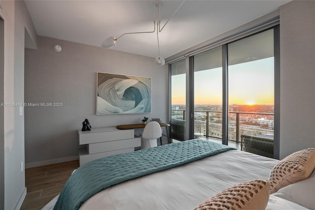 bedroom featuring access to exterior, floor to ceiling windows, baseboards, and wood finished floors