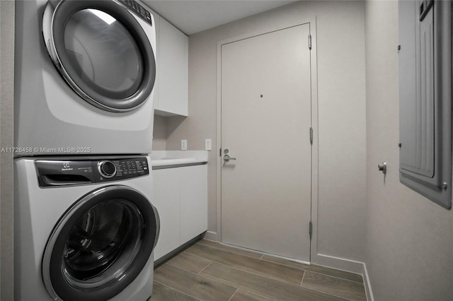 laundry area with stacked washer / drying machine, cabinet space, baseboards, and wood tiled floor