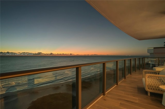 balcony at dusk featuring a water view