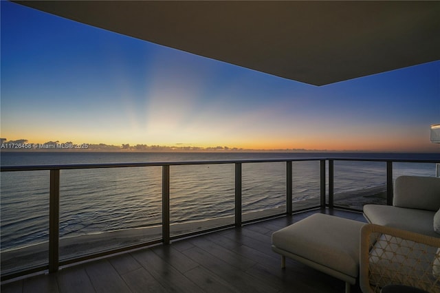 balcony at dusk featuring a water view