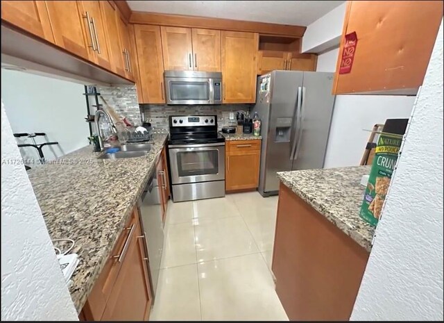 1621 Collins Ave Unit 310, Miami Beach, FL 33139 - kitchen with appliances with stainless steel finishes, light stone counters, decorative backsplash, brown cabinetry, and light tile patterned floors