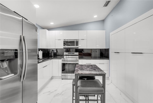 kitchen with vaulted ceiling, a center island, white cabinetry, appliances with stainless steel finishes, and a breakfast bar area