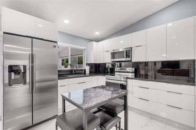 kitchen featuring vaulted ceiling, backsplash, sink, stainless steel appliances, and white cabinets