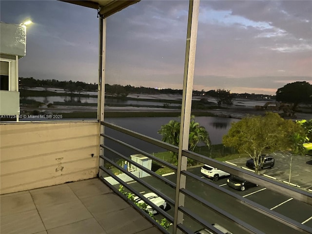 balcony at dusk featuring a water view