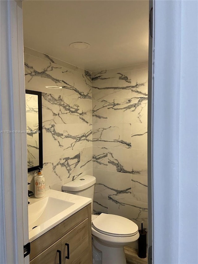 bathroom featuring toilet, tile walls, and vanity