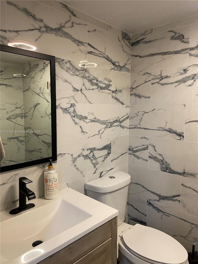 bathroom with toilet, vanity, and tile walls