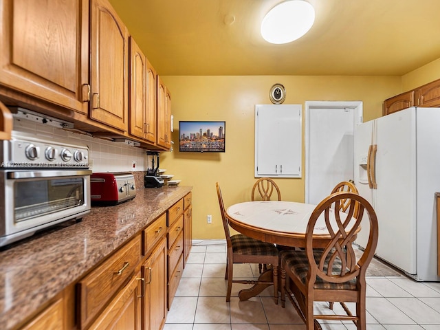 kitchen with decorative backsplash, light tile patterned floors, white refrigerator with ice dispenser, and dark stone countertops