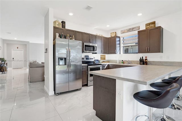 kitchen featuring kitchen peninsula, a breakfast bar area, appliances with stainless steel finishes, dark brown cabinetry, and sink