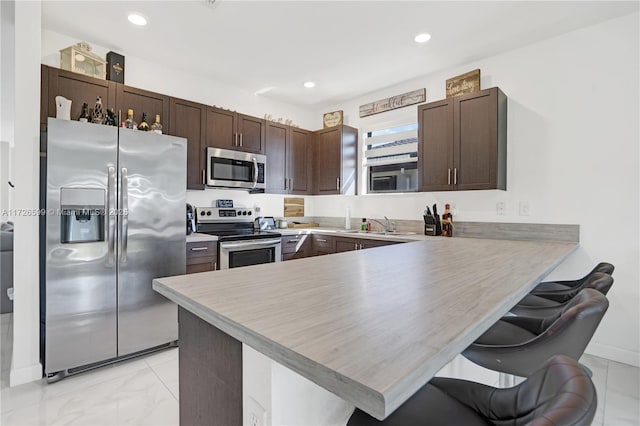 kitchen with a breakfast bar, kitchen peninsula, sink, stainless steel appliances, and dark brown cabinets