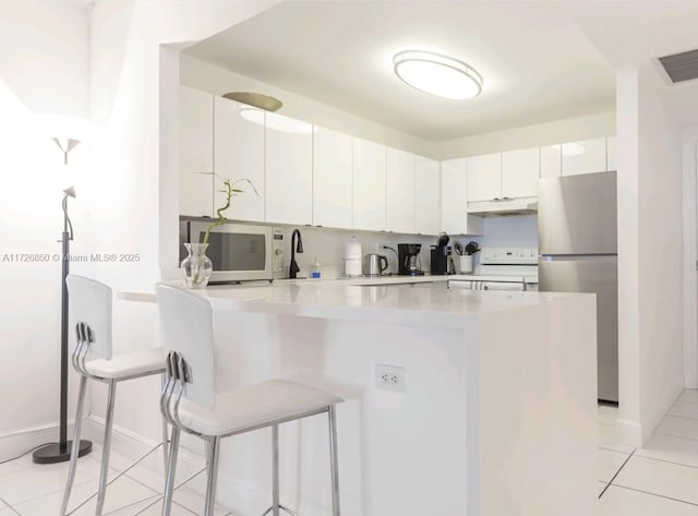 kitchen with white cabinets, light tile patterned floors, white appliances, and a breakfast bar area