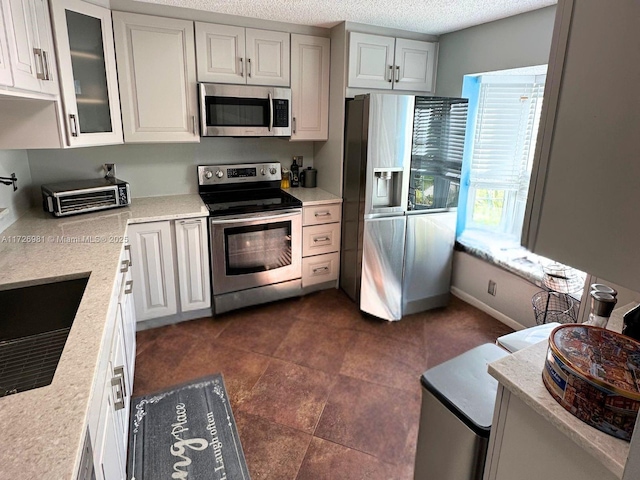 kitchen with appliances with stainless steel finishes, light stone countertops, glass insert cabinets, and white cabinets