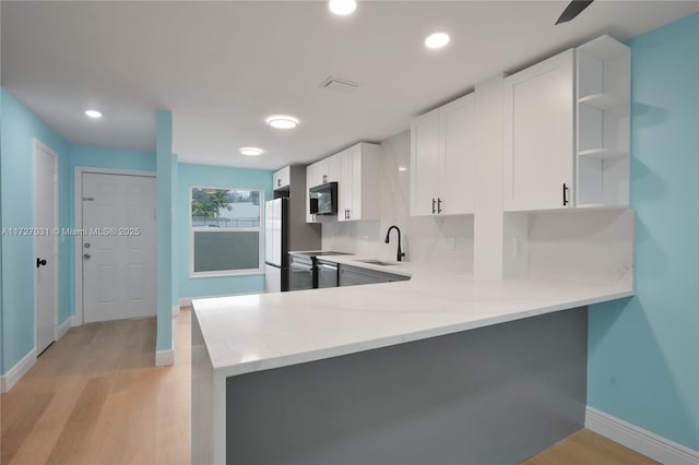 kitchen featuring kitchen peninsula, sink, white cabinets, light wood-type flooring, and decorative backsplash