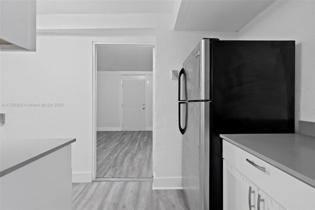 kitchen with white cabinets, light wood-type flooring, and stainless steel fridge