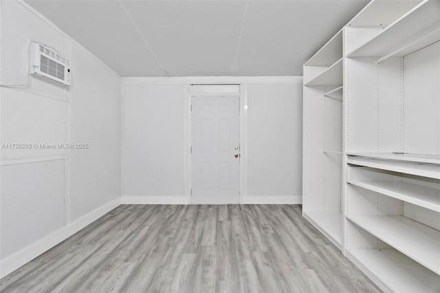 walk in closet featuring light wood-type flooring and an AC wall unit