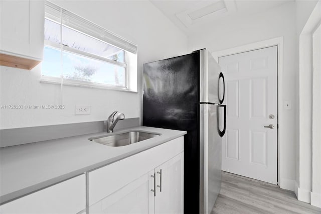 kitchen with light wood-type flooring, stainless steel fridge, white cabinets, and sink