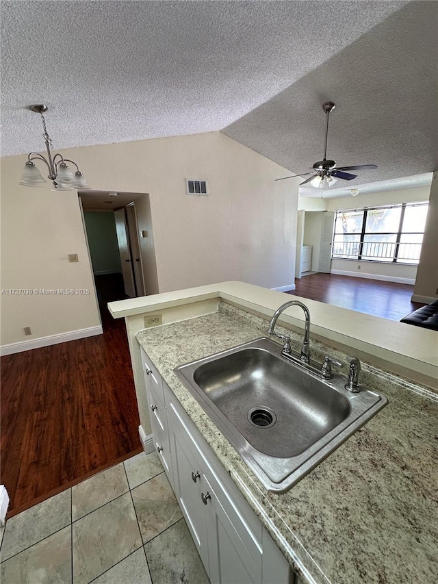 kitchen with ceiling fan with notable chandelier, lofted ceiling, white cabinetry, sink, and light tile patterned floors