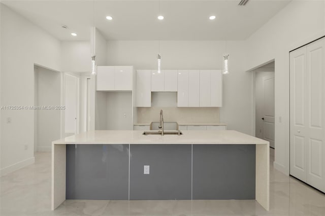 kitchen featuring decorative light fixtures, white cabinetry, tasteful backsplash, an island with sink, and sink