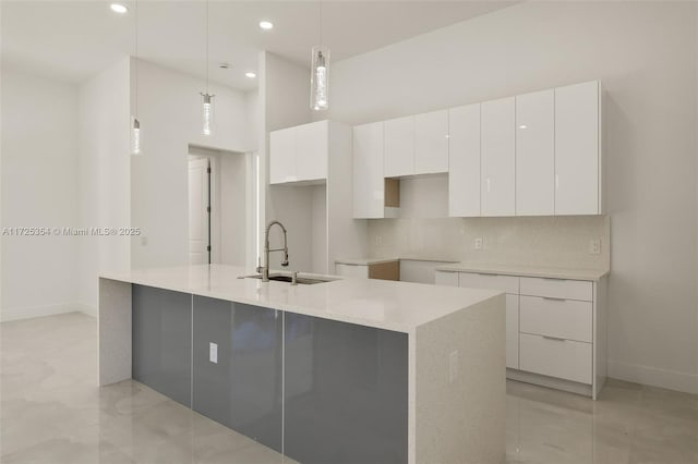 kitchen with tasteful backsplash, a center island with sink, sink, white cabinetry, and hanging light fixtures