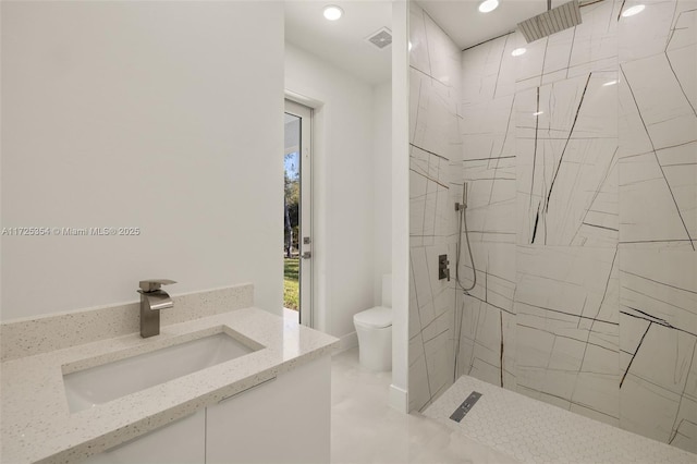 bathroom featuring toilet, tiled shower, and vanity