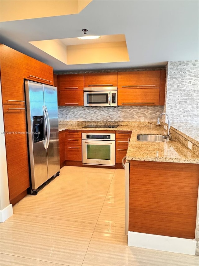 kitchen with light stone countertops, sink, a tray ceiling, and stainless steel appliances