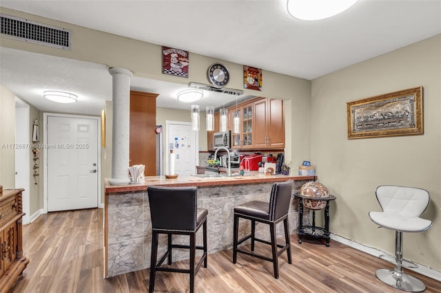 kitchen featuring pendant lighting, kitchen peninsula, wood-type flooring, sink, and a breakfast bar area