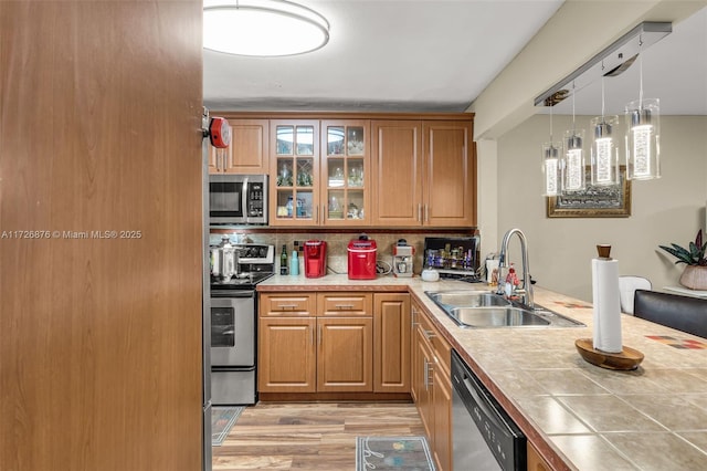 kitchen with tile counters, stainless steel appliances, sink, hanging light fixtures, and light wood-type flooring