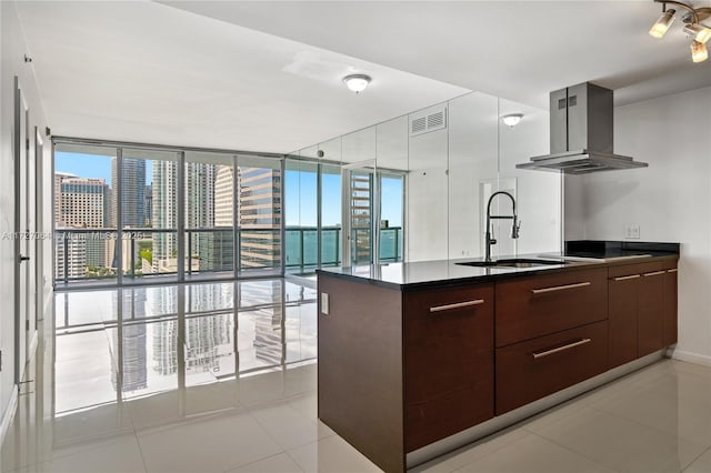 kitchen with island exhaust hood, light tile patterned floors, sink, dark brown cabinets, and expansive windows