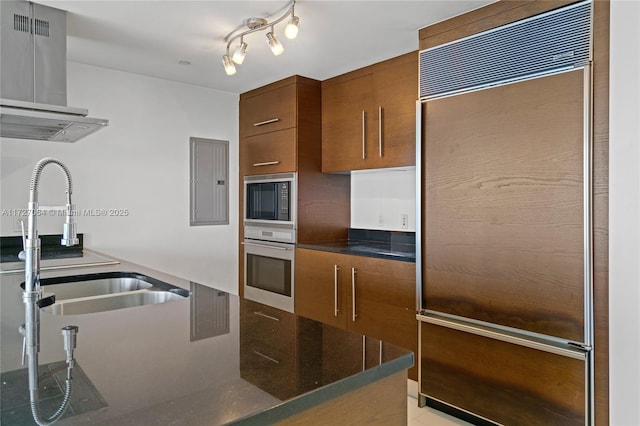 kitchen featuring built in appliances, range hood, electric panel, and sink