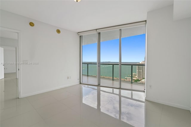 tiled empty room featuring a water view and floor to ceiling windows