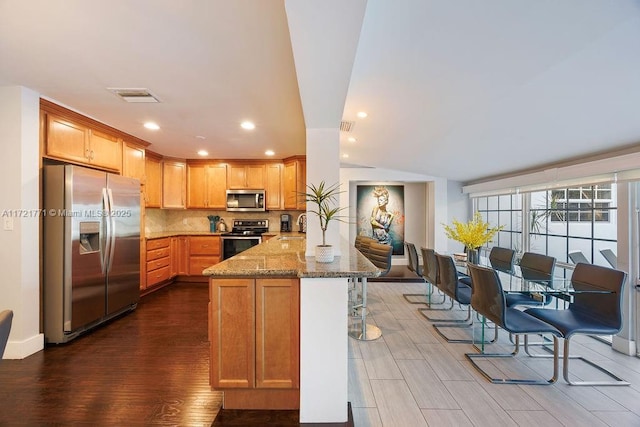 kitchen featuring appliances with stainless steel finishes, backsplash, dark hardwood / wood-style flooring, and light stone countertops