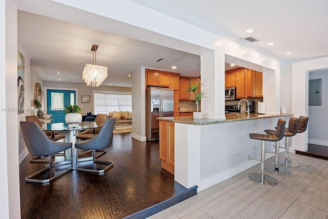 kitchen featuring appliances with stainless steel finishes, decorative light fixtures, kitchen peninsula, a chandelier, and light stone counters