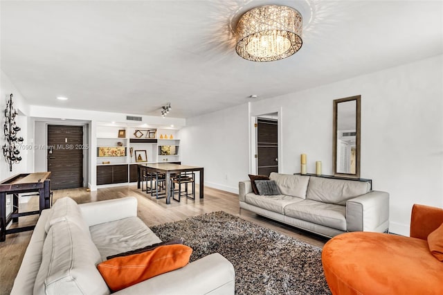 living room with built in features, light hardwood / wood-style flooring, and an inviting chandelier