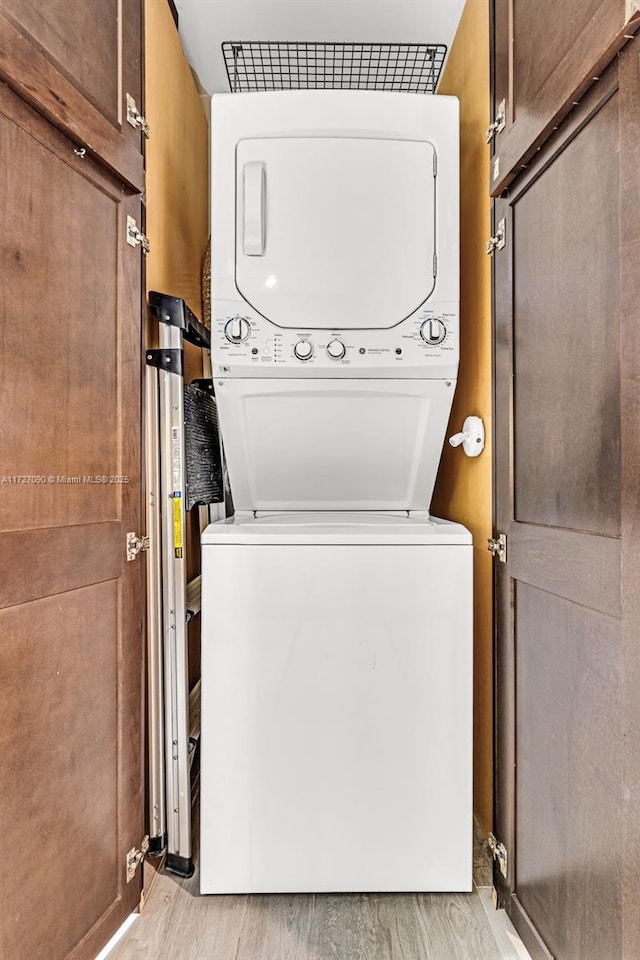 laundry area with light wood-type flooring, stacked washer and clothes dryer, and cabinets