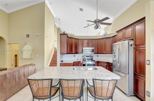 kitchen featuring sink, a breakfast bar area, appliances with stainless steel finishes, an island with sink, and light stone countertops