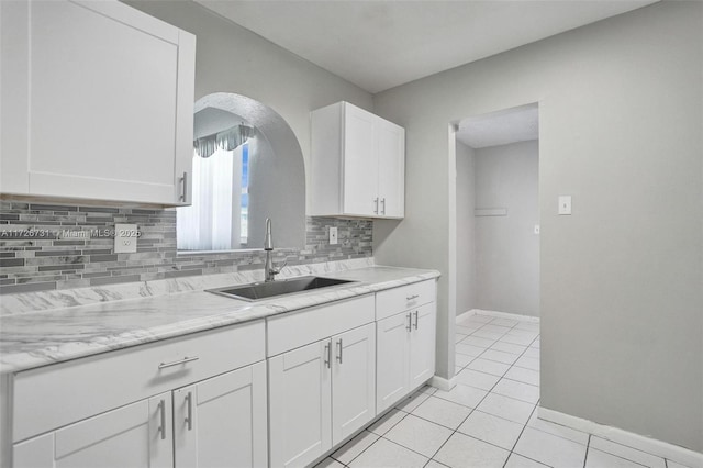 kitchen featuring tasteful backsplash, light tile patterned flooring, white cabinets, light stone counters, and sink