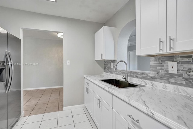 kitchen featuring sink, light tile patterned floors, light stone countertops, stainless steel fridge with ice dispenser, and white cabinets