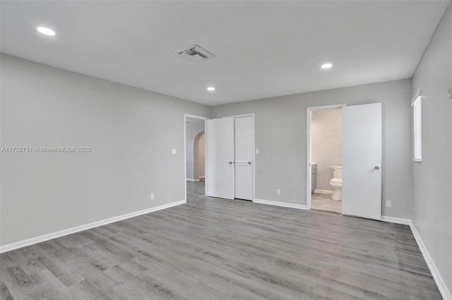 unfurnished bedroom with ensuite bathroom and light hardwood / wood-style floors