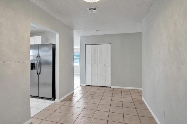 interior space featuring light tile patterned floors, stainless steel fridge, white cabinetry, and a textured ceiling